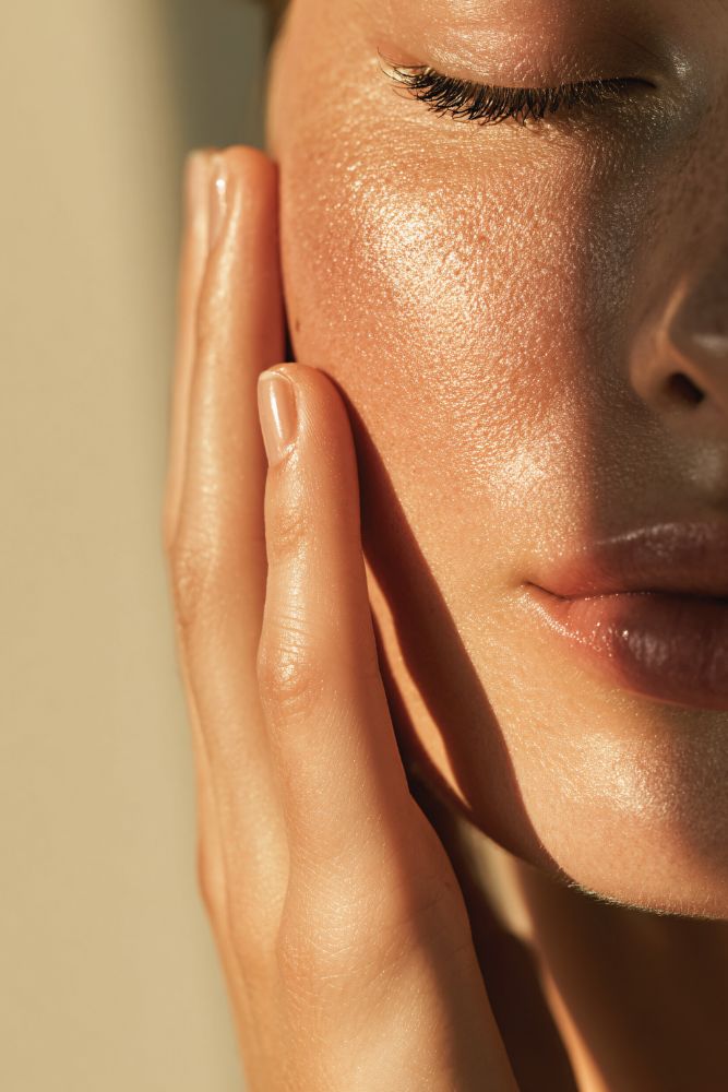 Close-up of a person's face with hand on cheek against a beige background
