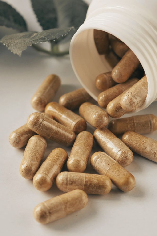 Brown capsules spilling out of a white container on a light surface