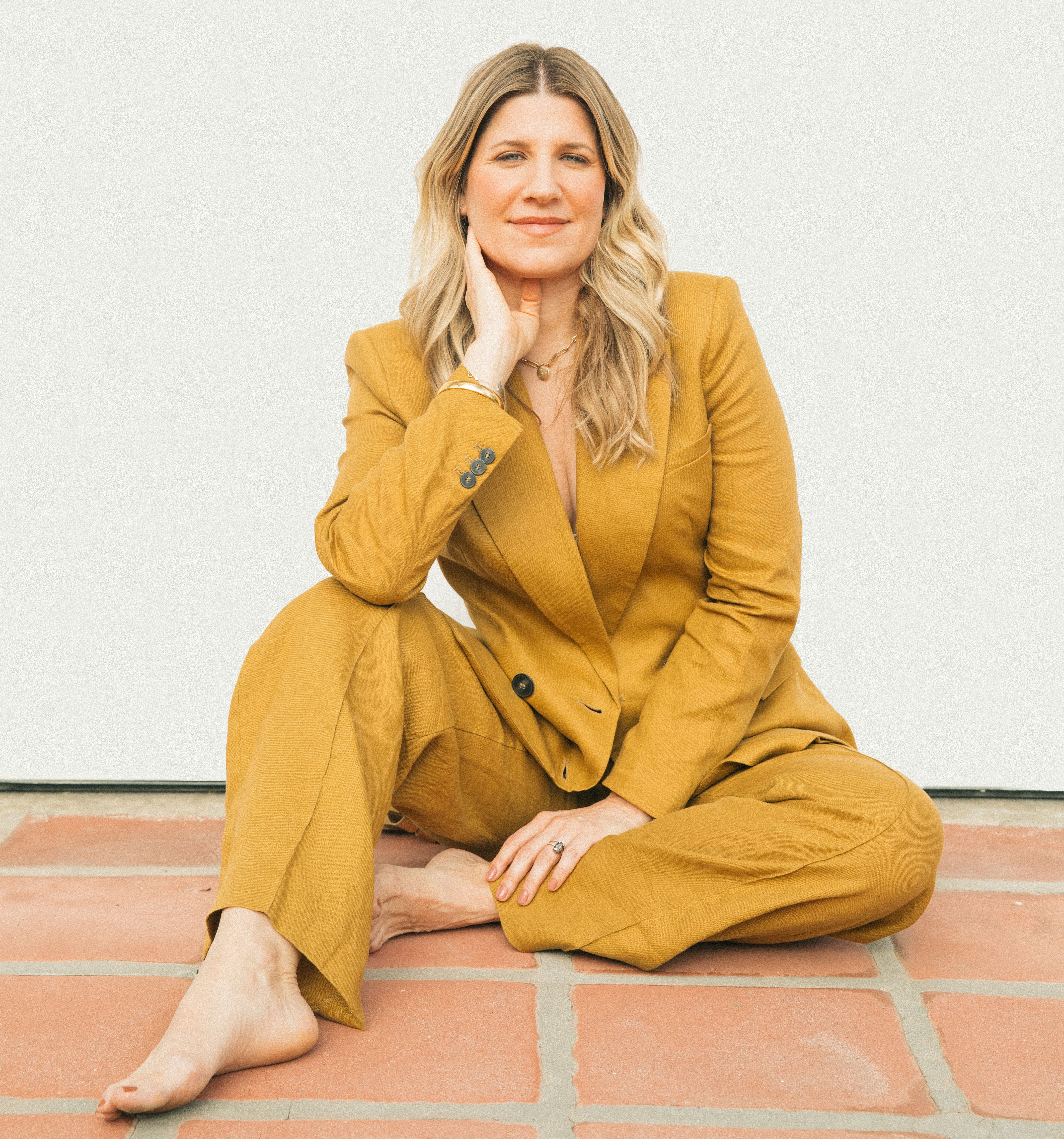 Woman in a mustard yellow suit sitting on a tiled floor.