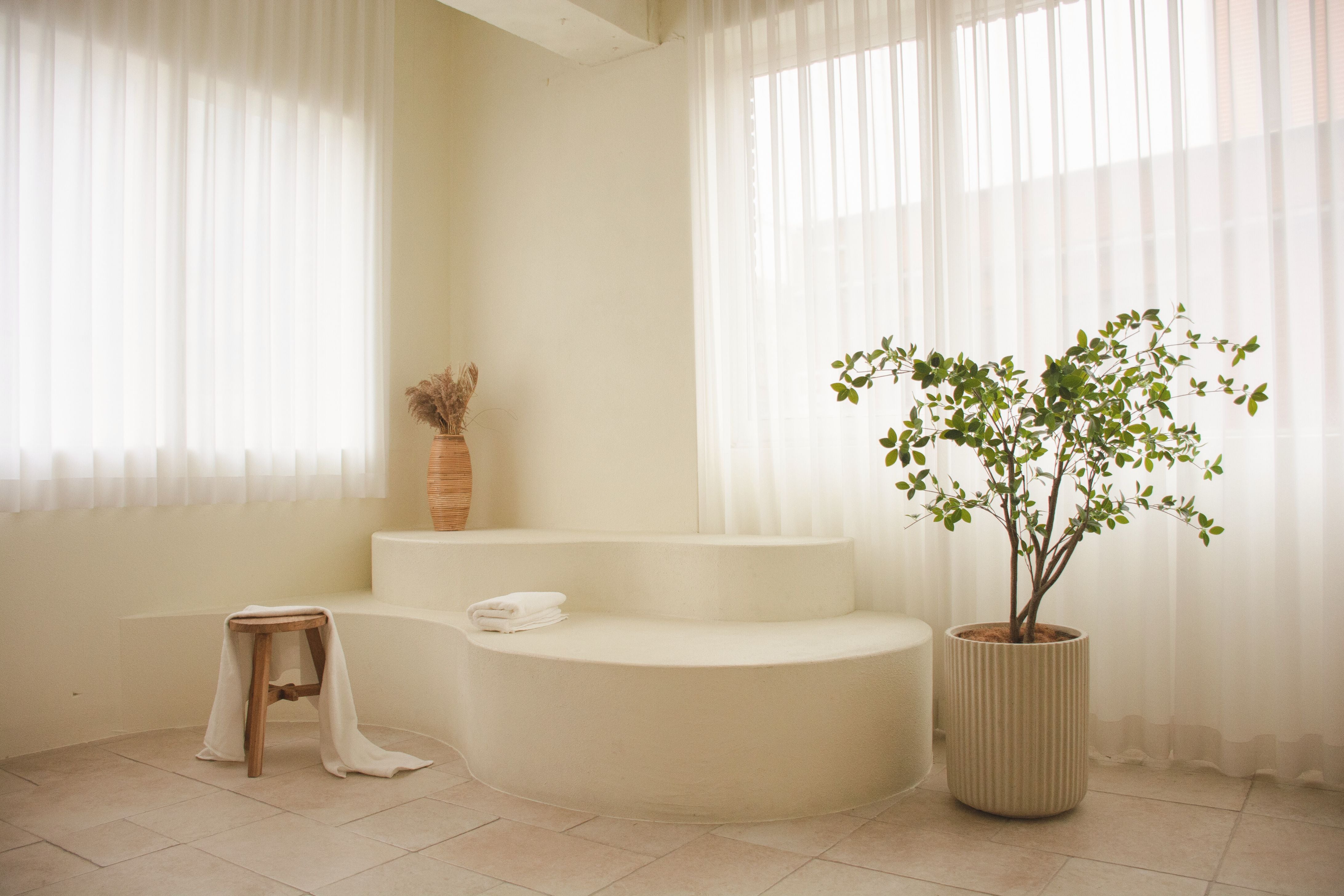 Modern bathroom with a freestanding bathtub, potted plants, and sheer curtains.