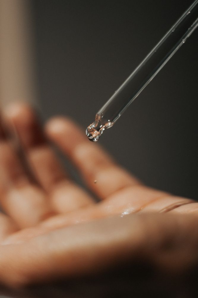 Dropper with a drop of liquid held above a hand on a dark background