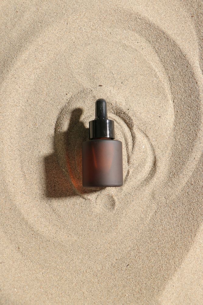 Skincare dropper bottle on sand with concentric circles